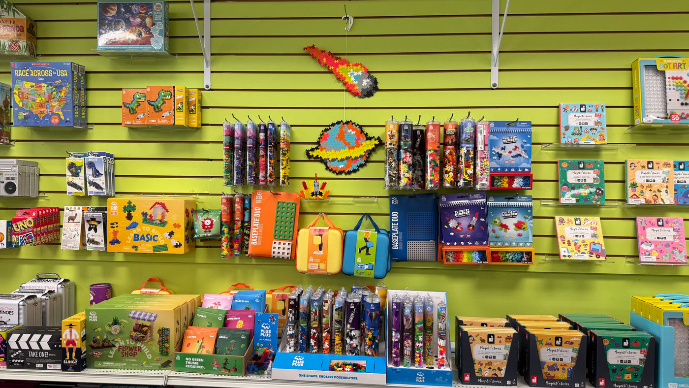 Display of children's toys and games on a green slat wall in a store.